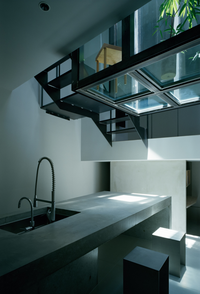 Kitchen counter with concrete island and cantilevered glass skylight bridge above with greenery