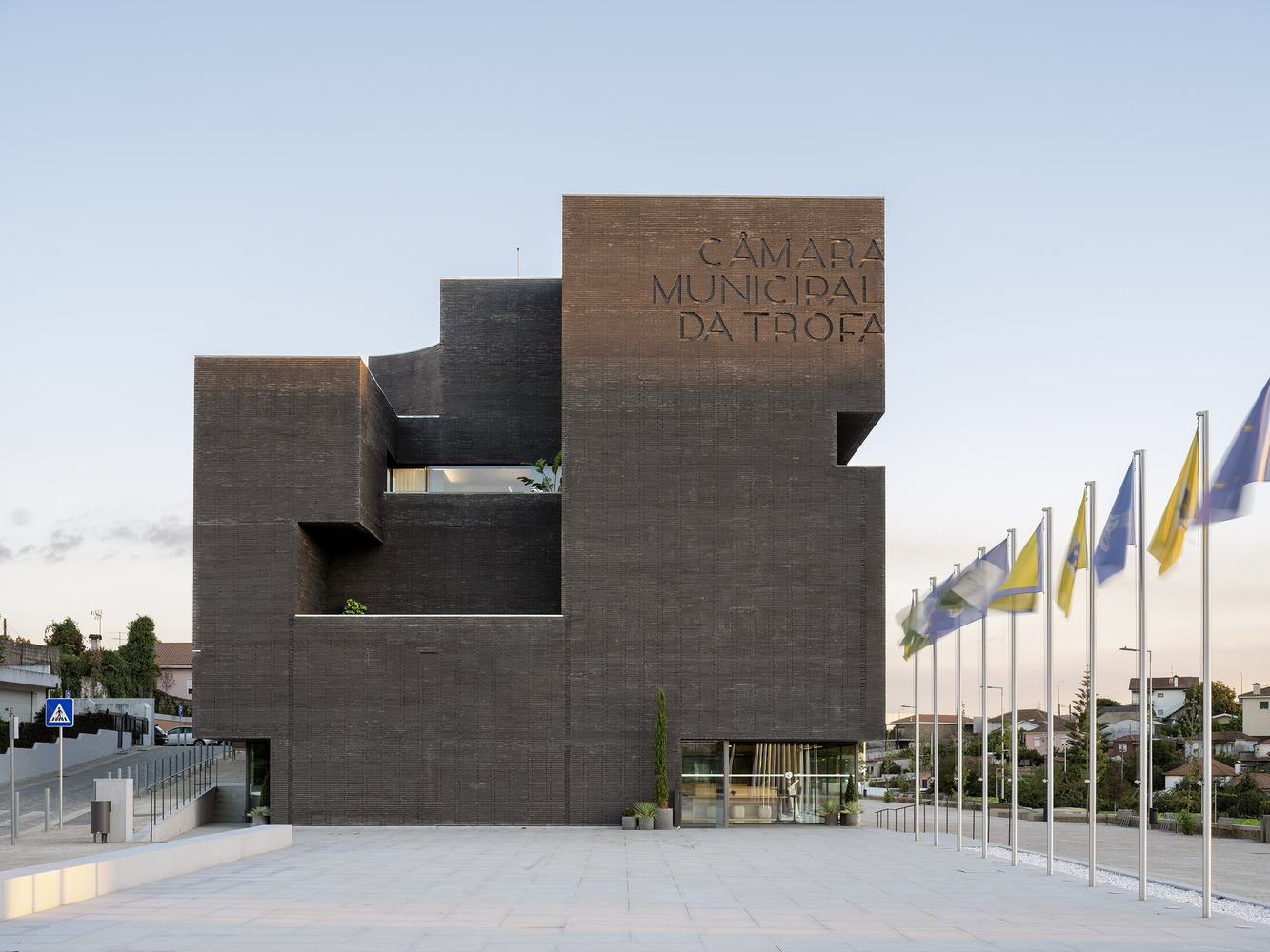Front plaza with row of flags and dark brick facade inscribed with lettering