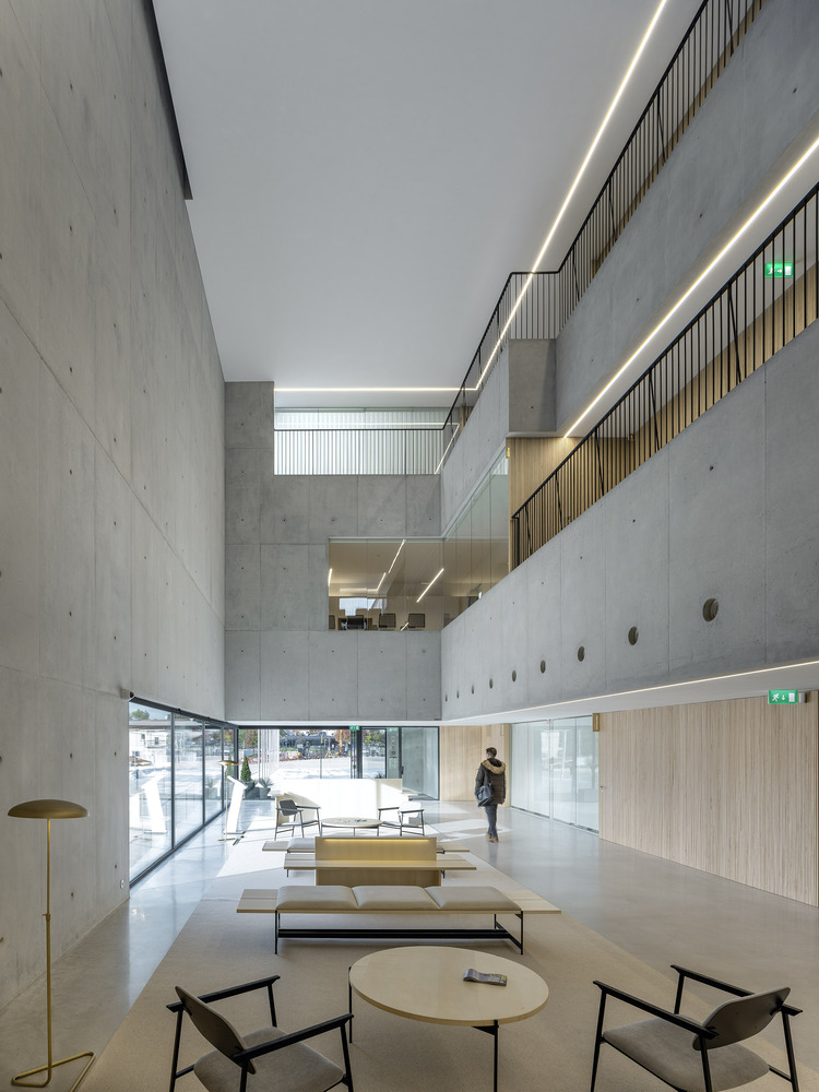Triple-height concrete entrance lobby with clerestory lighting and timber-clad reception desk below suspended balconies