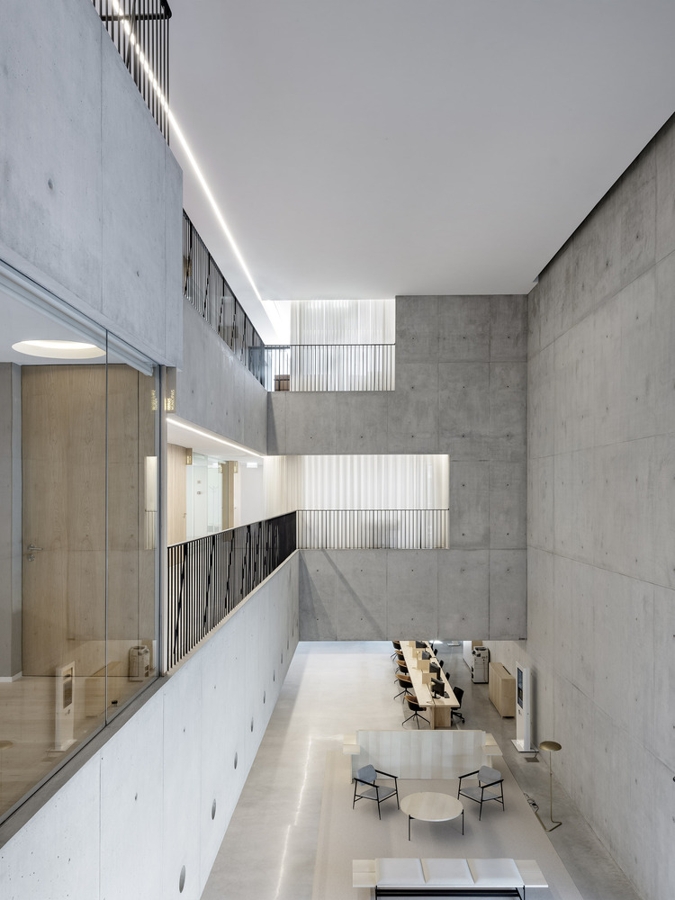 Multi-level atrium with board-formed concrete walls, glass balustrades, and reading tables at ground level