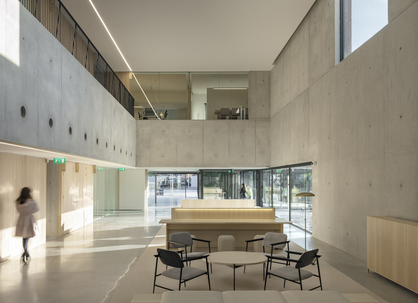 Double-height atrium with cast-in-place concrete walls and a blurred figure crossing the polished floor
