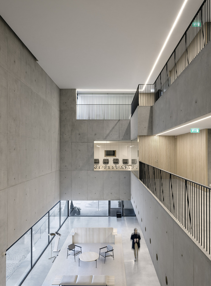 Multi-story atrium with board-formed concrete walls, timber-lined balconies and a person walking below