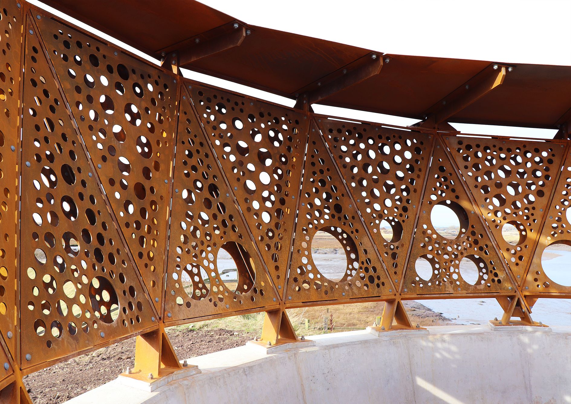 Perforated steel panels create a dynamic interplay of light and shadow at Greatham Creek Seal Hide, enhancing its sustainable design.