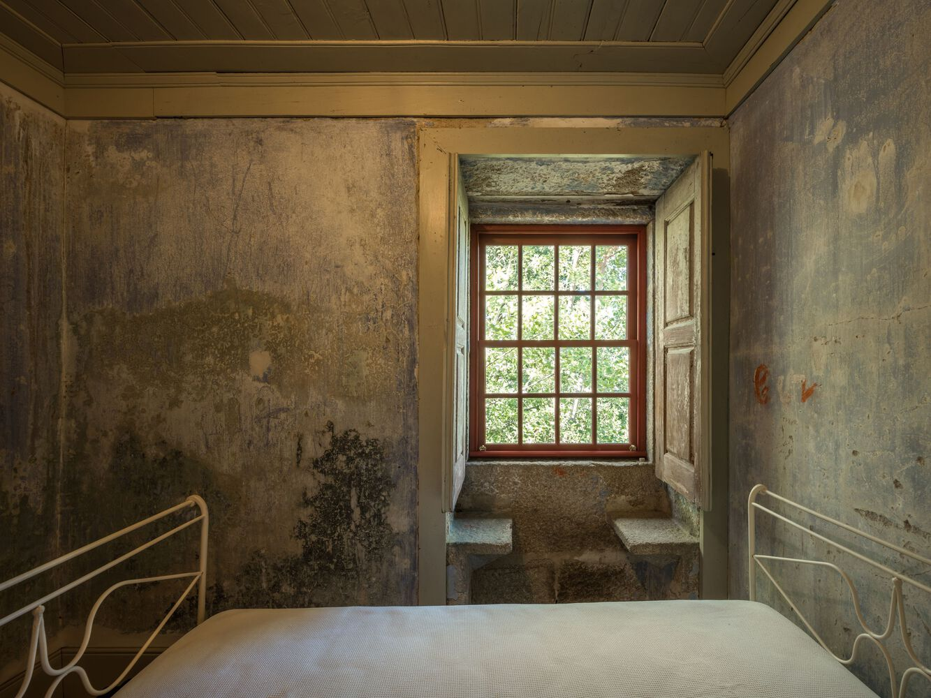 Bedroom with distressed plaster walls and deep window alcove looking onto trees