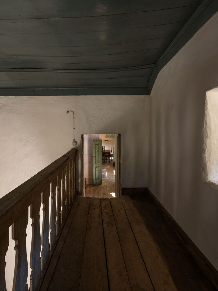 Timber balustrade along a narrow hallway with whitewashed walls and dark stained ceiling boards
