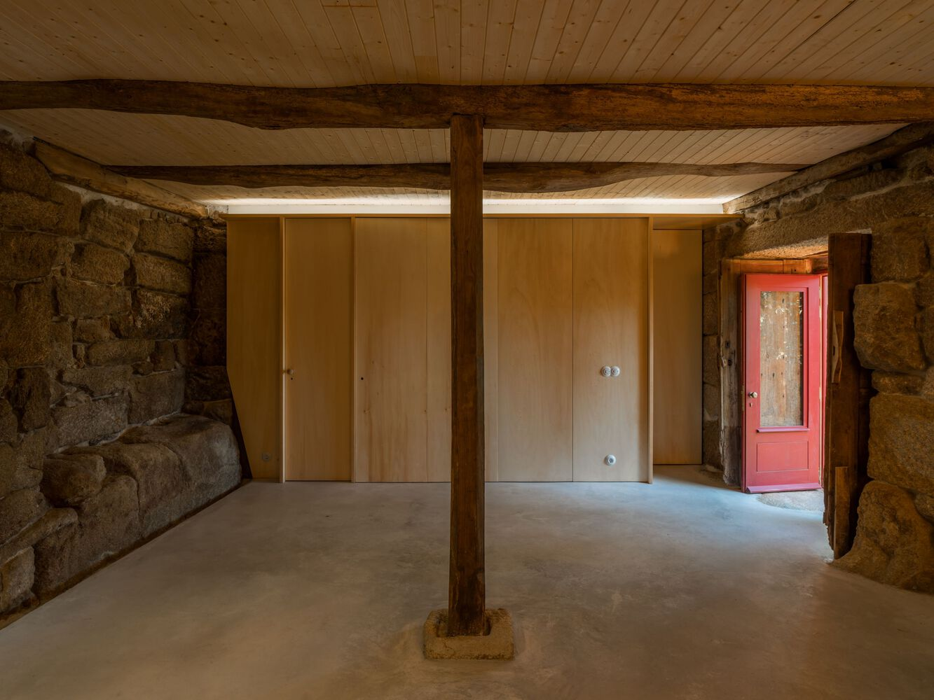 Interior room with plywood partition walls flanked by granite masonry and timber post on concrete floor