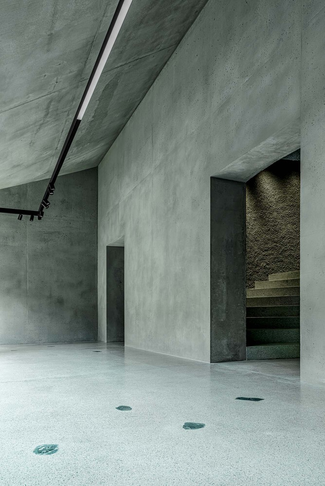 Concrete stairwell opening with exposed treads visible beyond a freestanding wall and angled ceiling