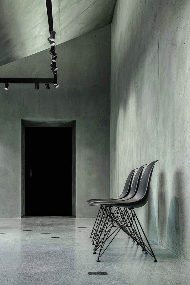 Interior corridor with board-formed concrete walls, stacked wire-frame chairs and black track lighting overhead
