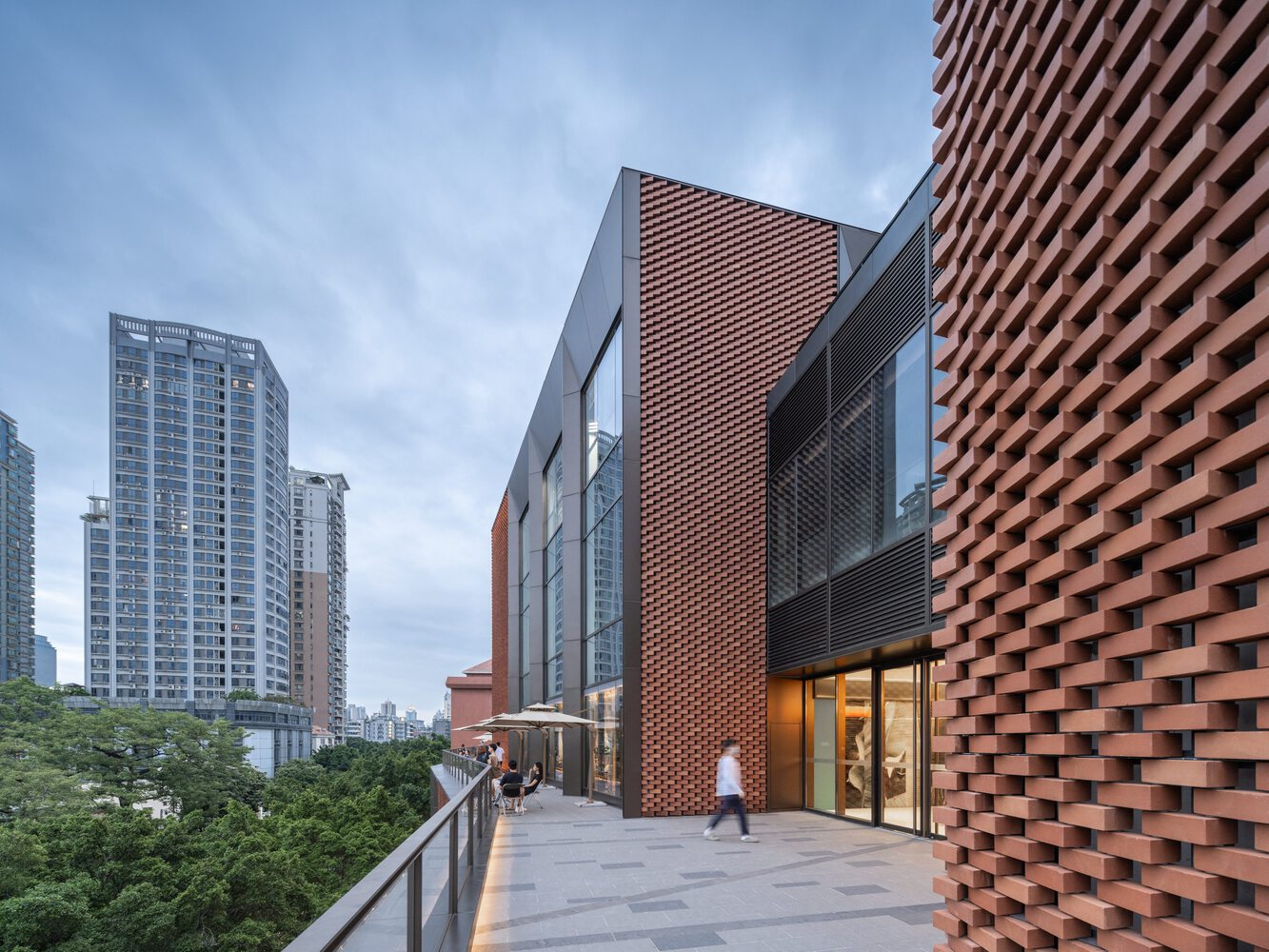Elevated terrace with terracotta screen walls and people walking at twilight under cloudy skies