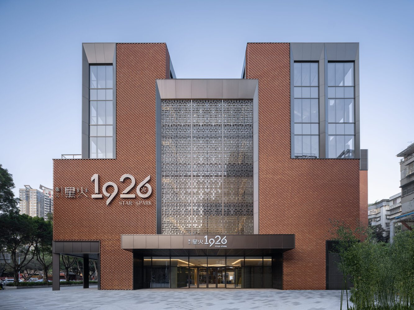 Main entrance facade featuring perforated screen panels flanked by terracotta brick volumes with illuminated date numerals