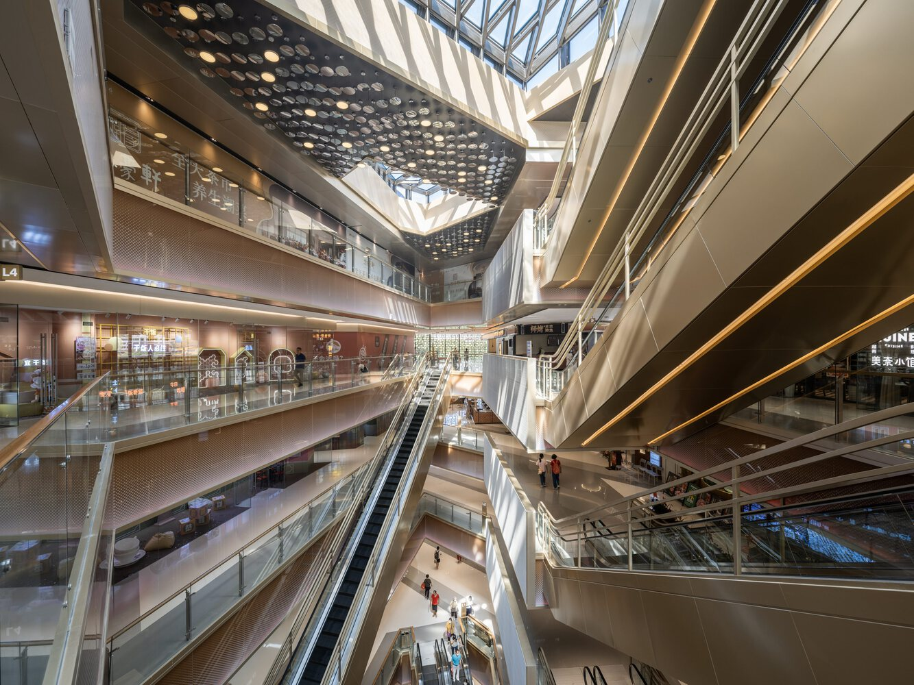 Multi-story atrium with escalators, perforated ceiling screen and daylight filtering through the glass roof above