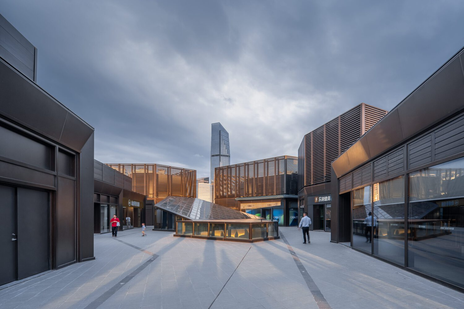 Rooftop courtyard with wooden pavilion surrounded by terracotta screens and shop fronts at dusk