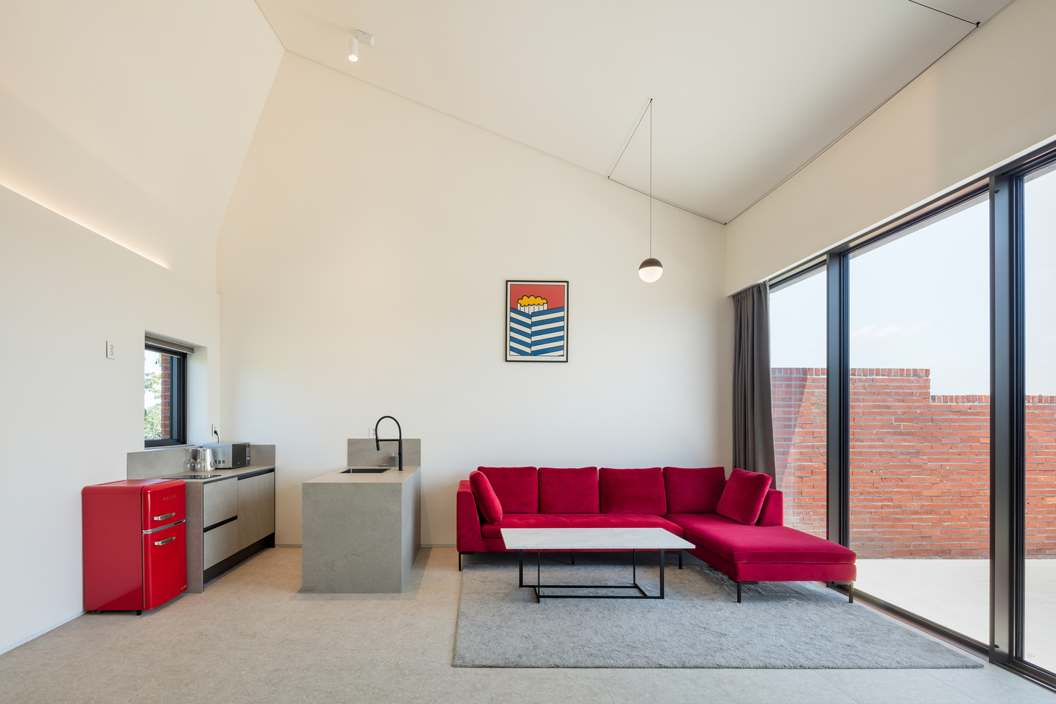 Living space with vaulted ceiling and concrete island overlooking a red brick courtyard through glazed doors