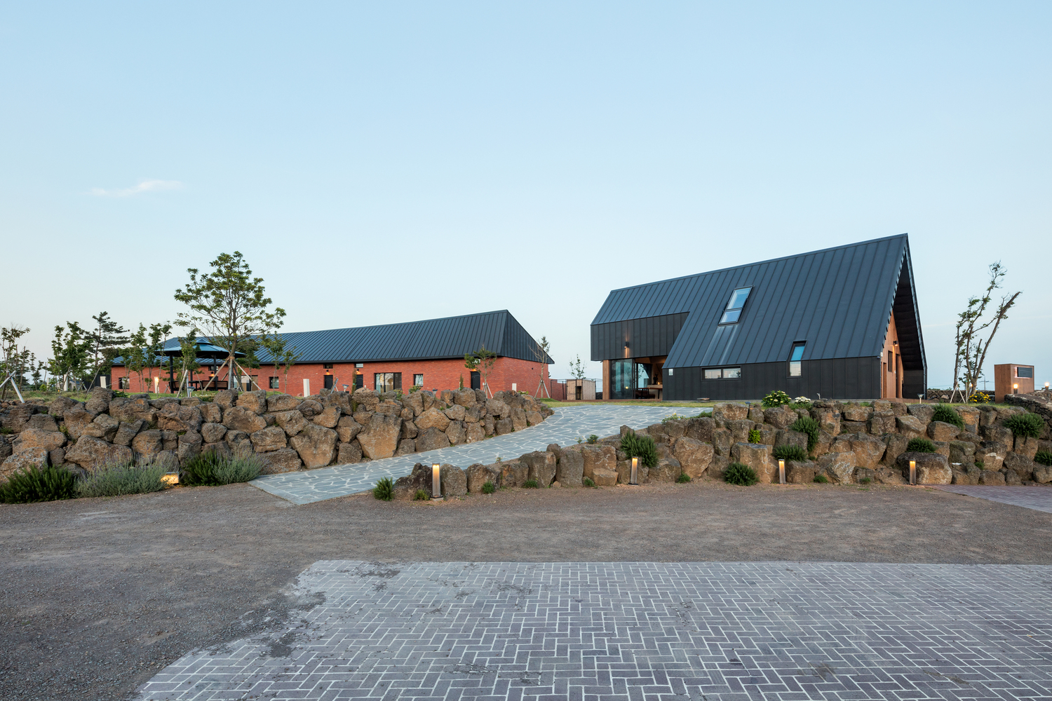 Paved entry plaza with volcanic rock retaining wall leading to clustered gabled volumes