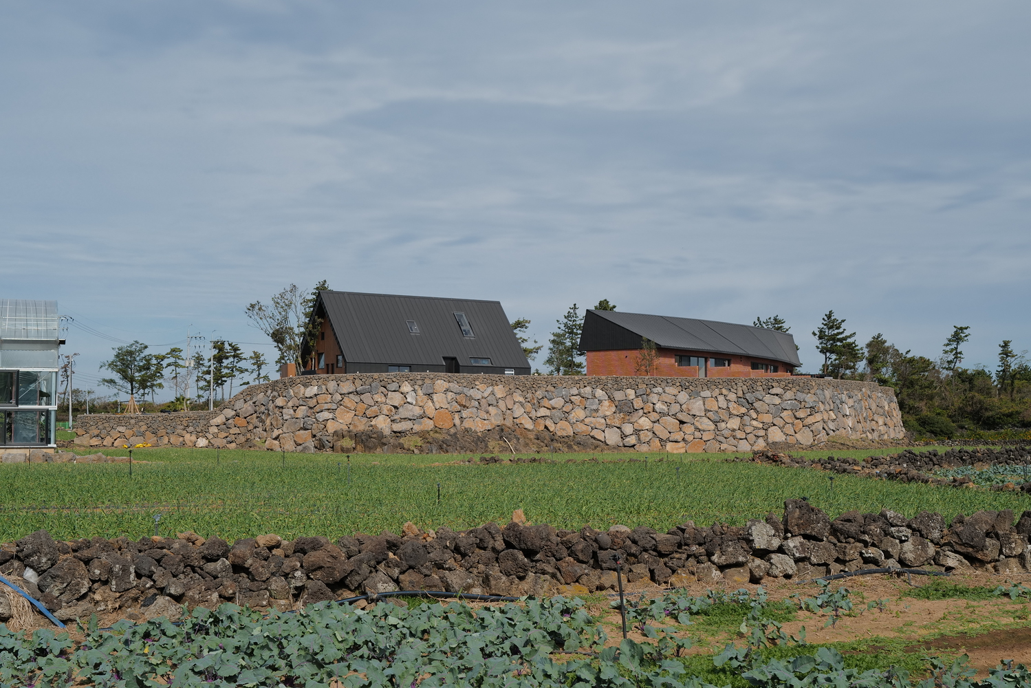 Two dark-roofed volumes atop a stone retaining wall rising from terraced agricultural fields