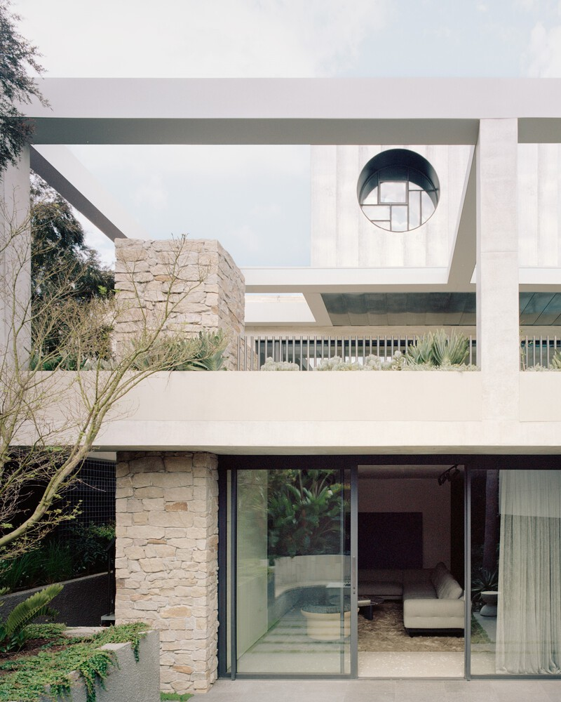 Stacked volumes with circular skylight puncturing cantilevered roof slab above stone-clad walls