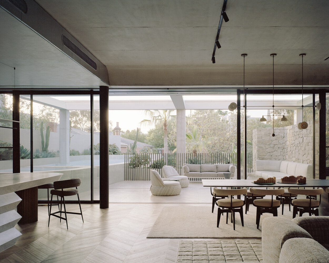 Open living and dining space with herringbone oak flooring overlooking poolside terrace at dusk