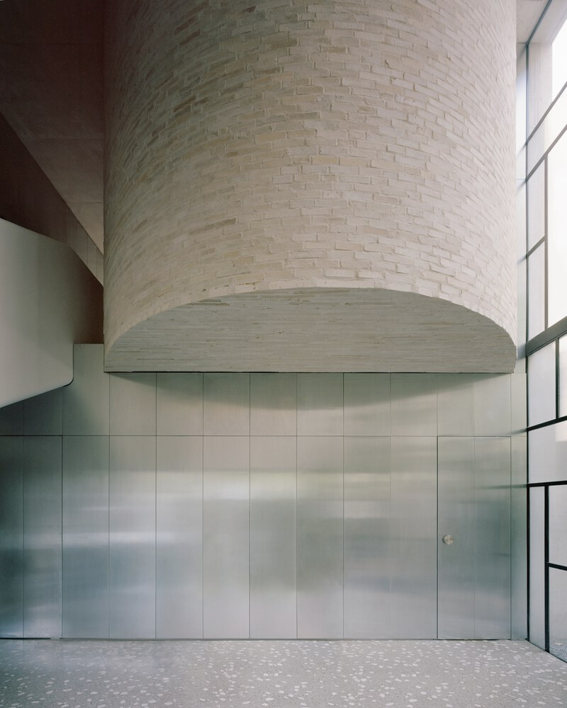 Curved stone masonry chimney rising above brushed metal cabinet wall and terrazzo floor