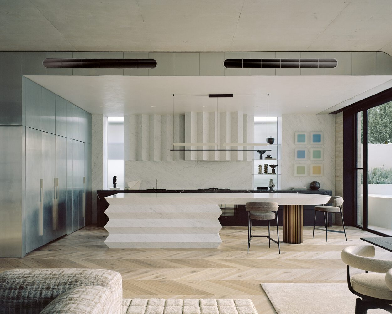 Kitchen island with sculptural plaster base beneath striped wall panels and chevron parquet flooring
