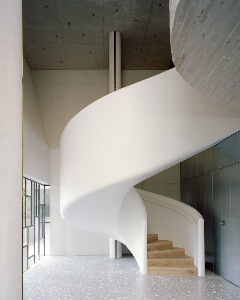 White sculptural spiral staircase with timber treads beneath an exposed concrete ceiling