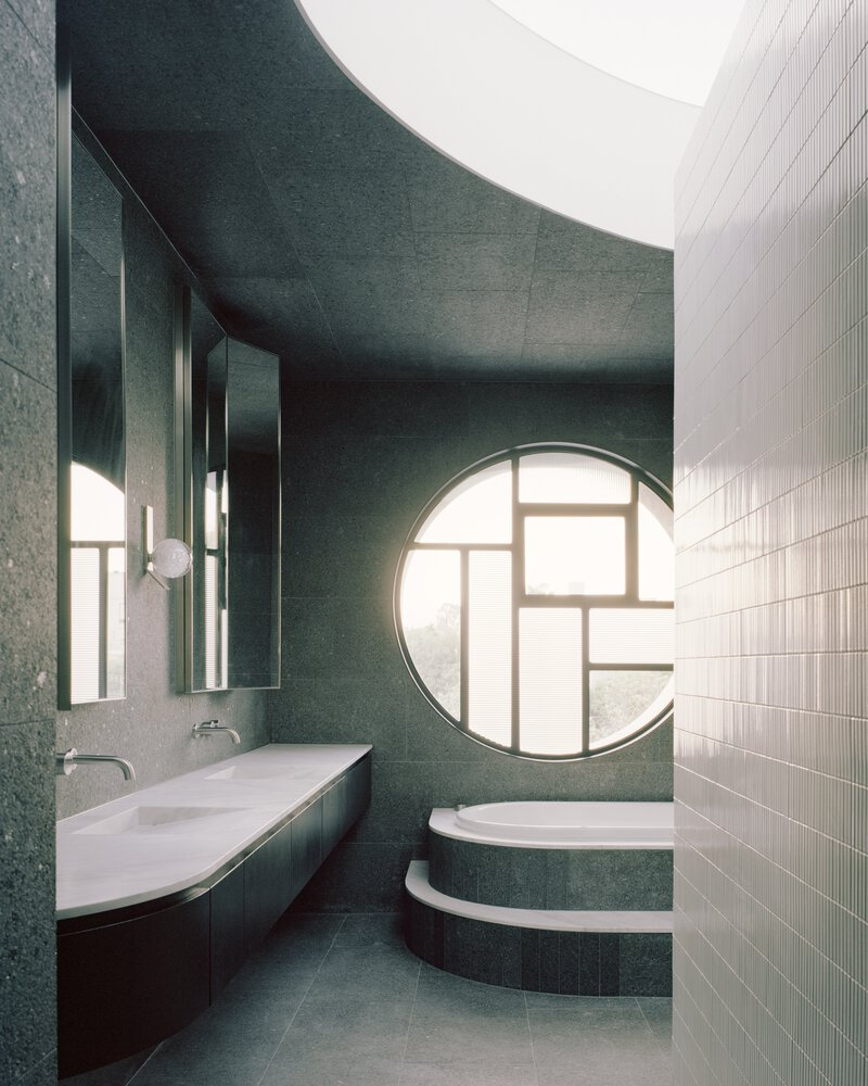 Bathroom with green terrazzo walls, circular window and stepped tub under a curved ceiling