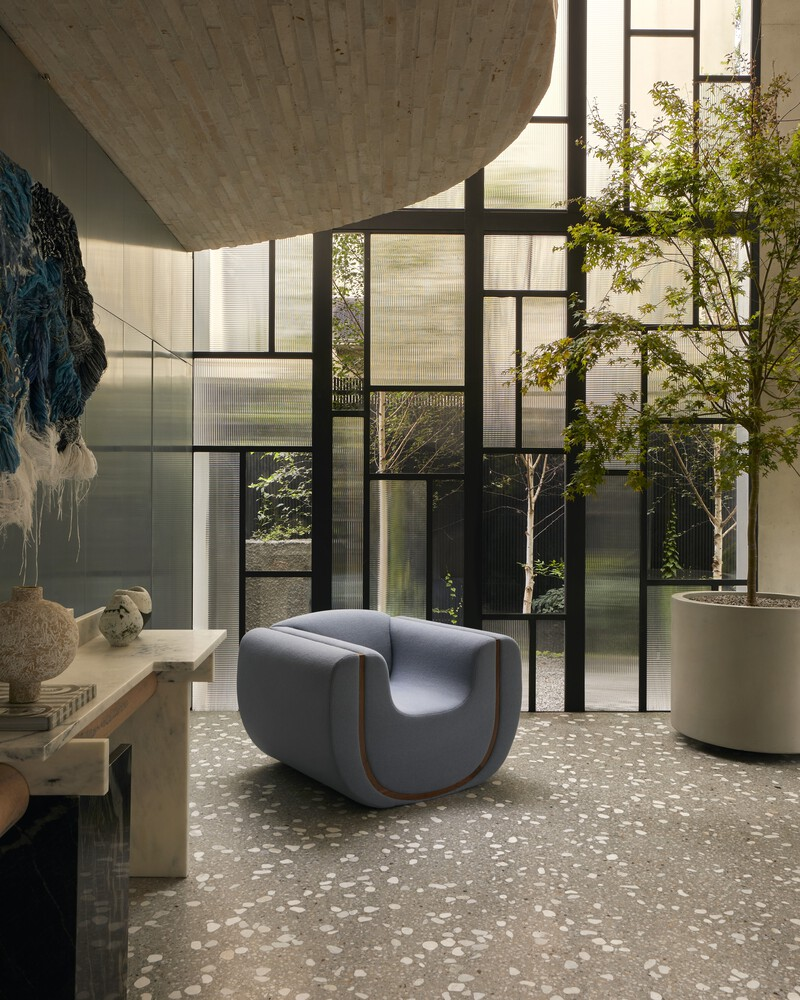 Interior courtyard view through black steel-framed glazing with planted trees in terrazzo planters
