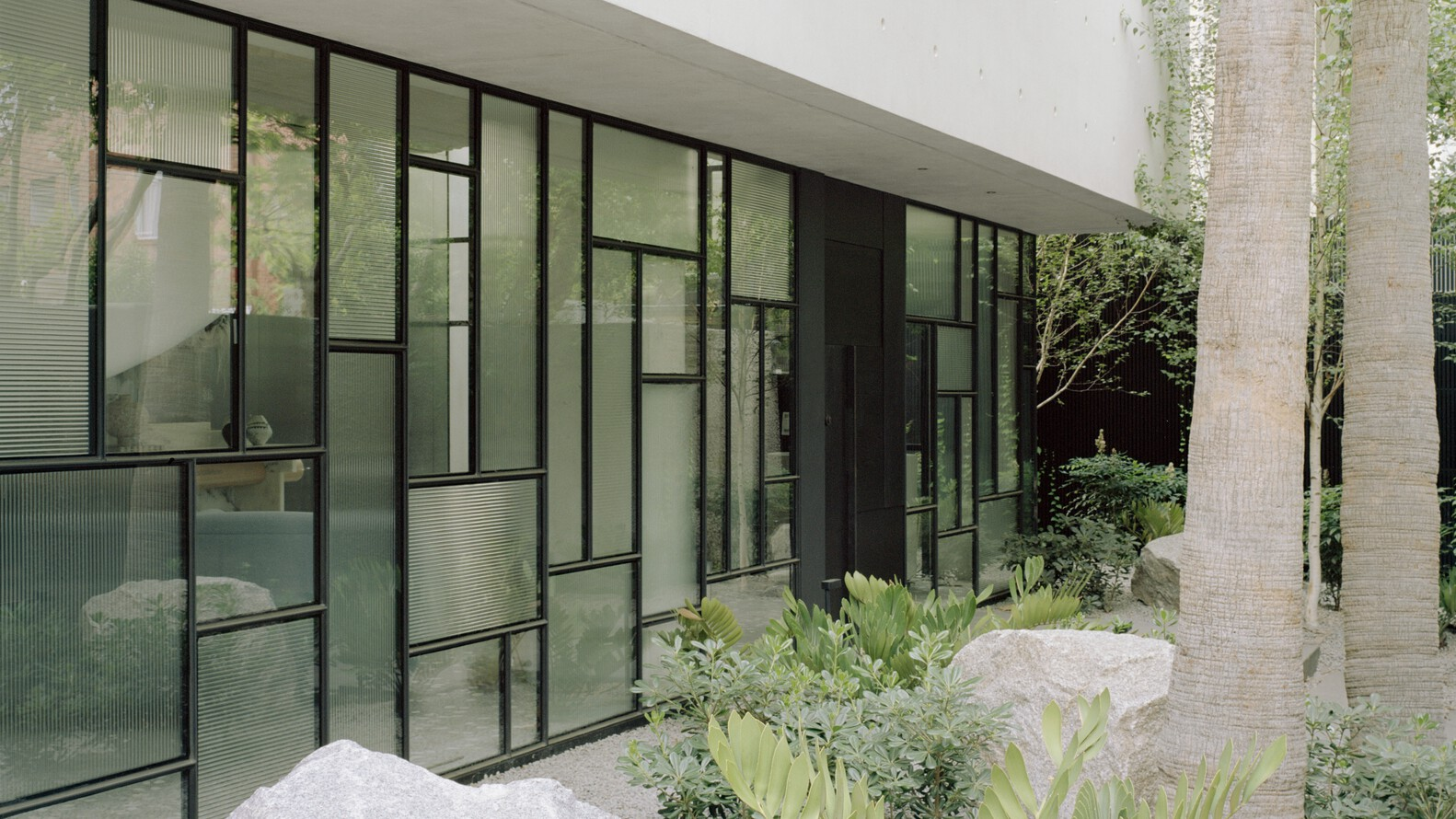 Exterior facade with irregular grid of steel-framed glazing and planted beds with rocks