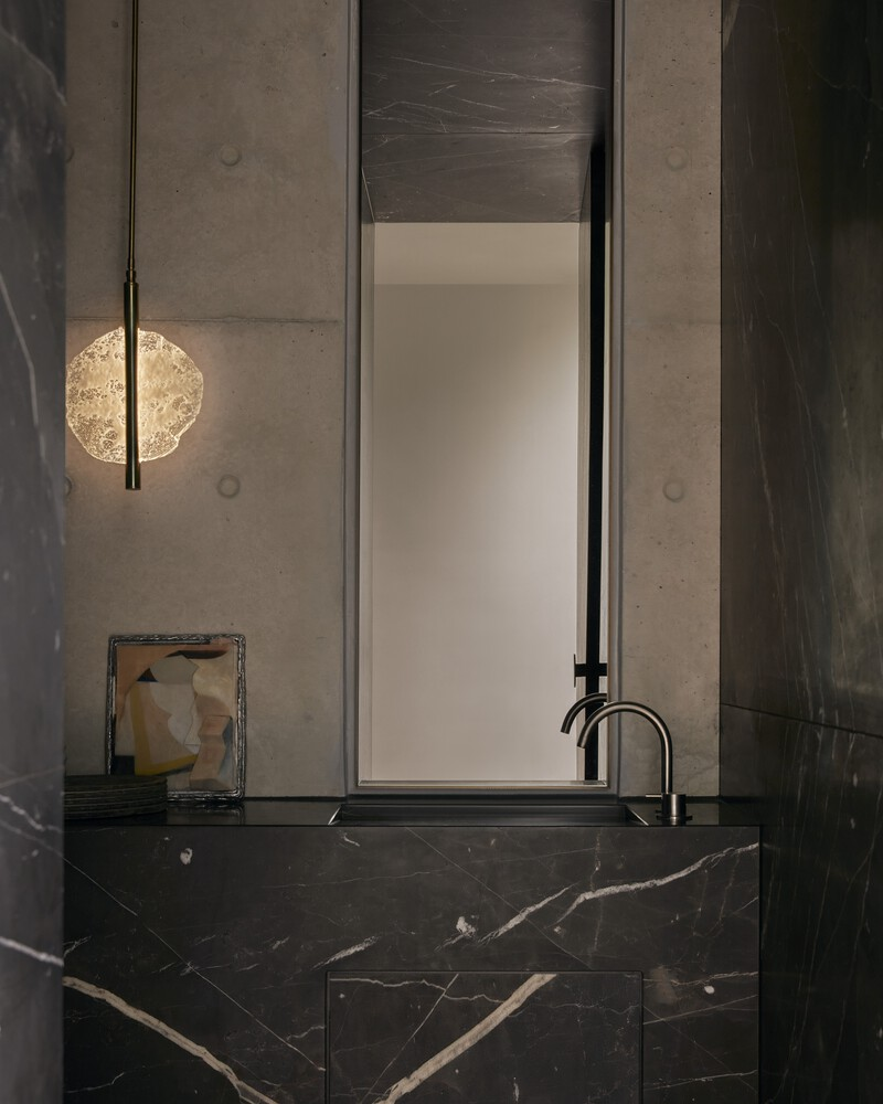 Black marble vanity with integrated basin and tall mirror flanked by cast concrete walls