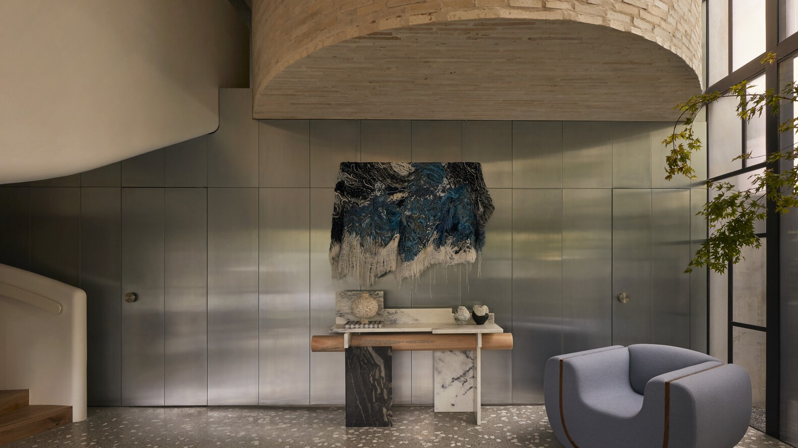 Brushed metal panel wall beneath a curved timber ceiling canopy with a potted tree nearby