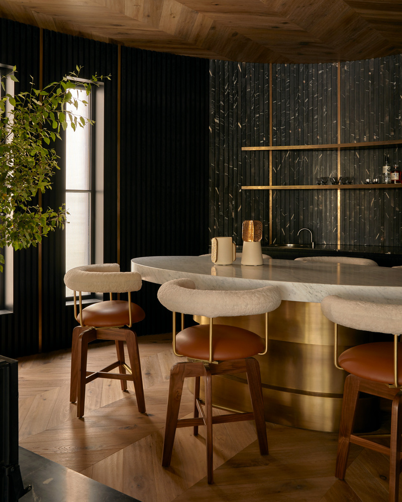 Bar counter clad in brass with upholstered stools under a herringbone timber ceiling