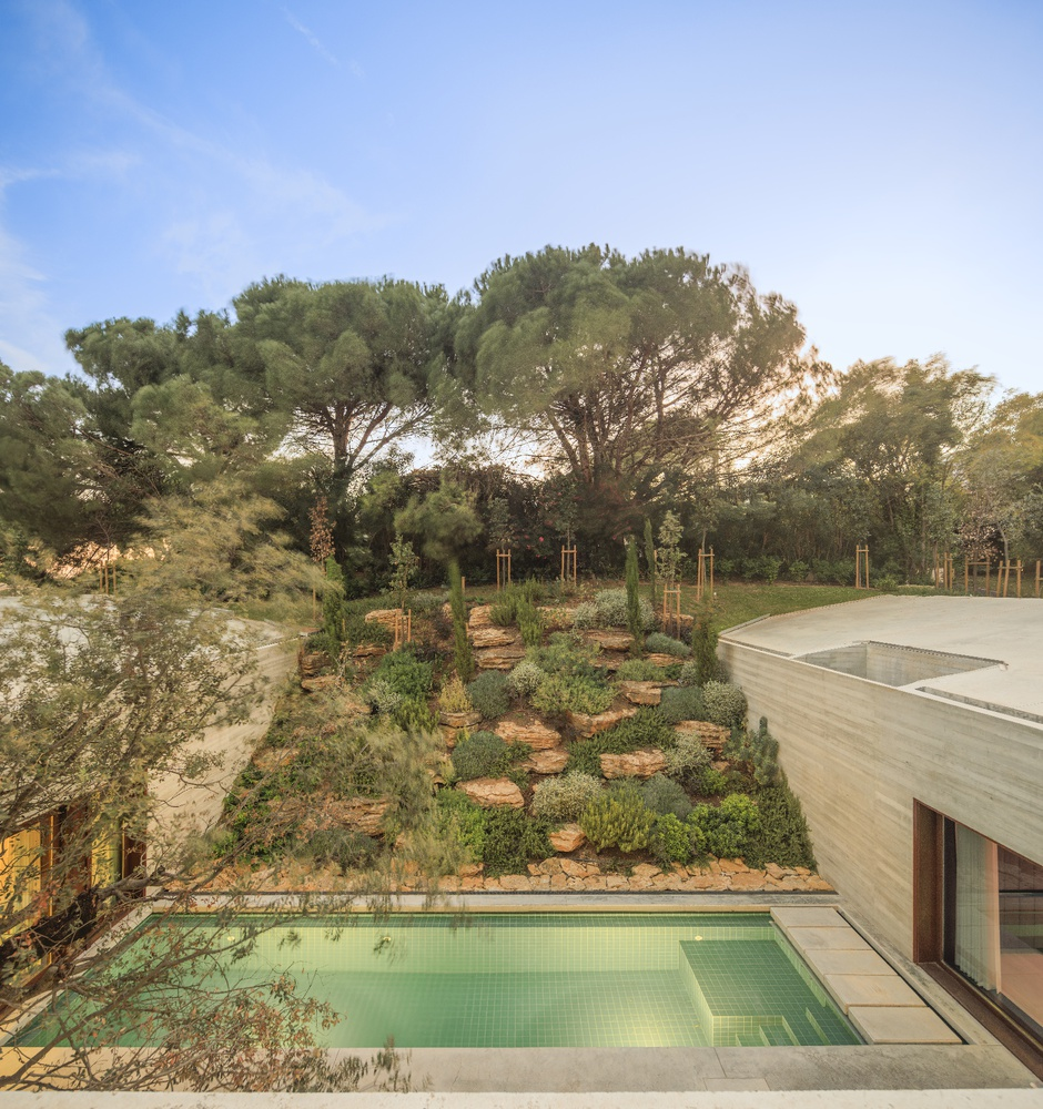 View across the planted hillside terraces and lap pool toward the concrete roof at golden hour
