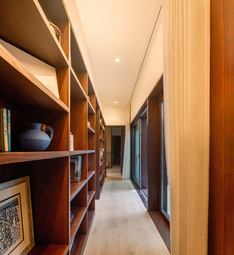 Corridor with built-in timber shelving along one wall and textured linen curtains on the opposite side
