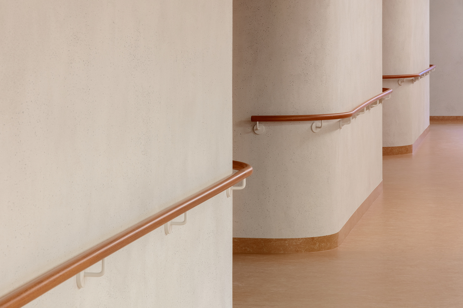 Curved corridor with timber handrails mounted on white walls and continuous rubber base trim