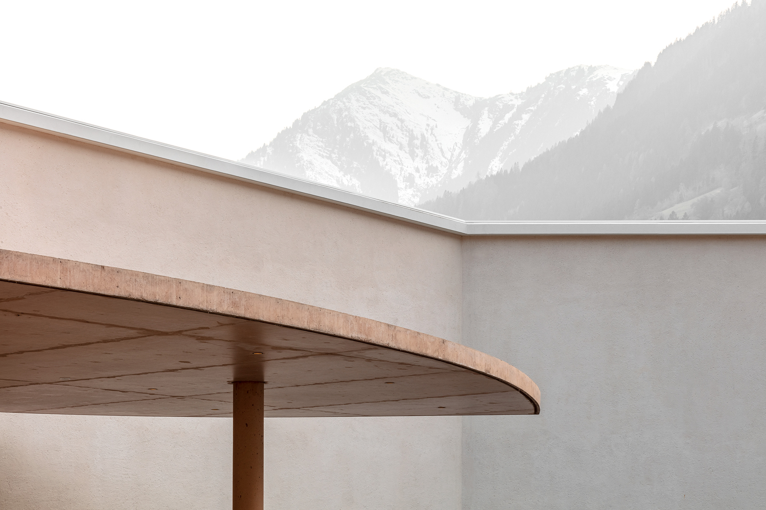 Cantilevered canopy with timber soffit and exposed edge against snow-dusted alpine peaks