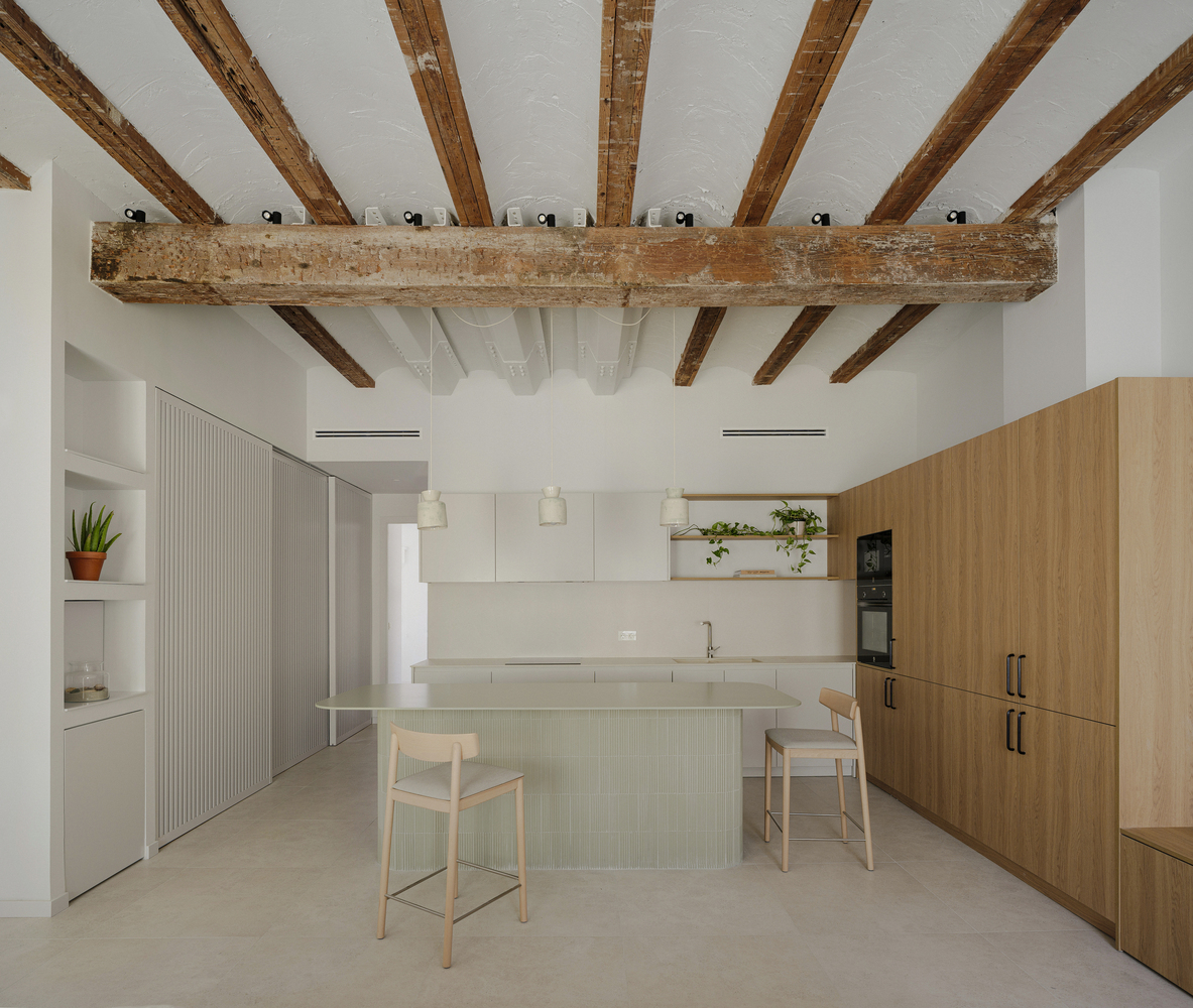 Kitchen with exposed timber ceiling beams, island with two stools, and white and wood cabinetry