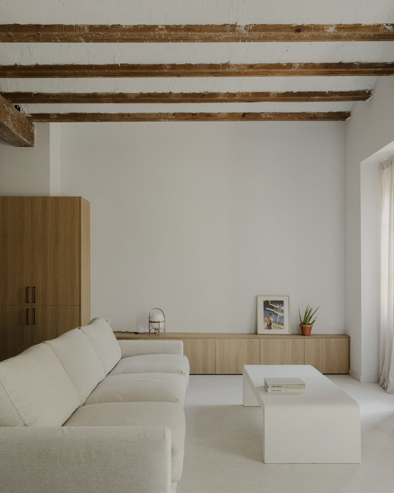 Living room with exposed timber ceiling beams, low sofa, and timber sideboard in soft natural light