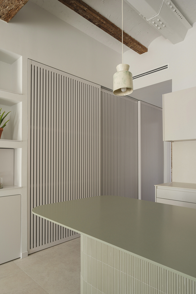 Fluted partition wall with integrated counter beneath exposed timber beams and white vaulted ceiling