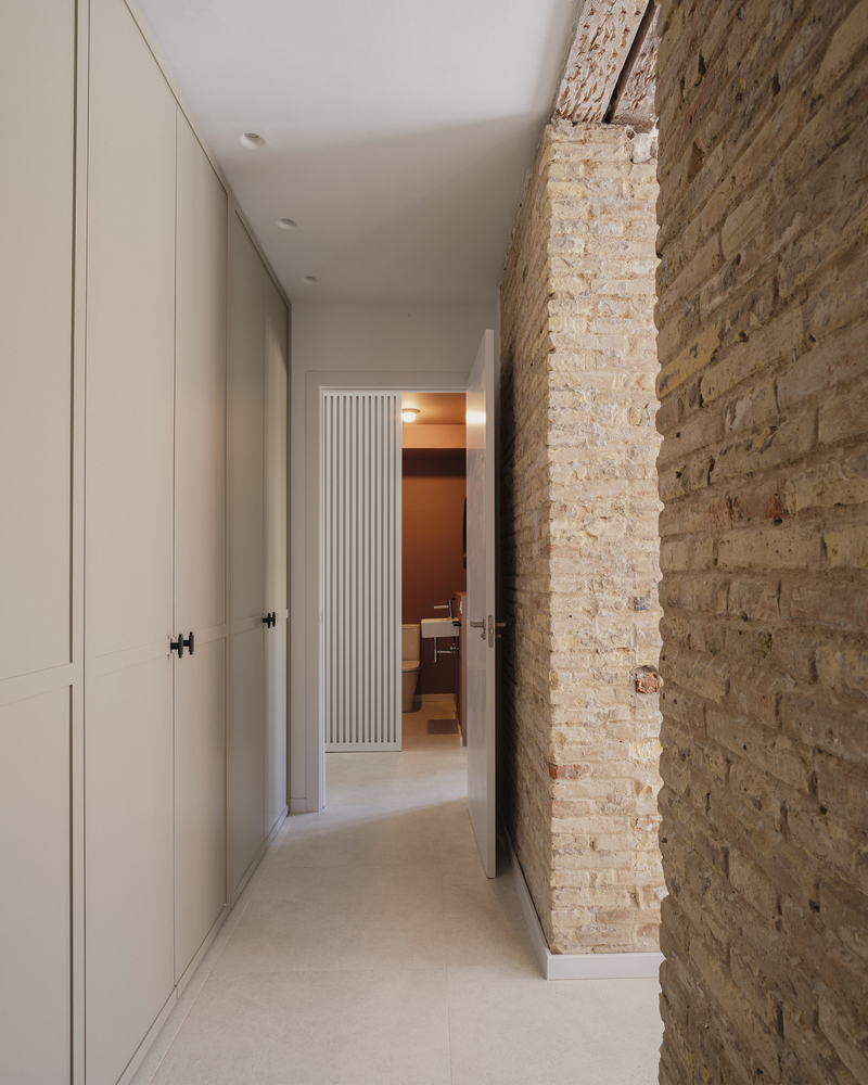 Narrow hallway with white cabinetry and exposed weathered brick wall leading toward fluted doorway