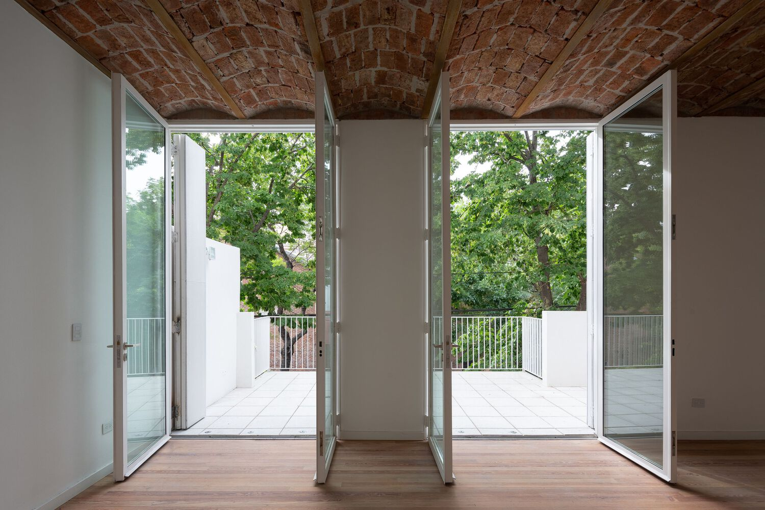 Room with exposed brick barrel vault ceiling opening to twin balconies framed by glass doors