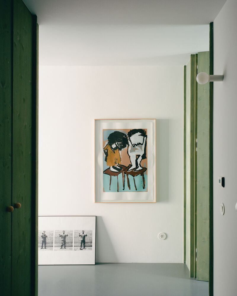 Interior corner with green timber door frames and framed artworks leaning against white walls