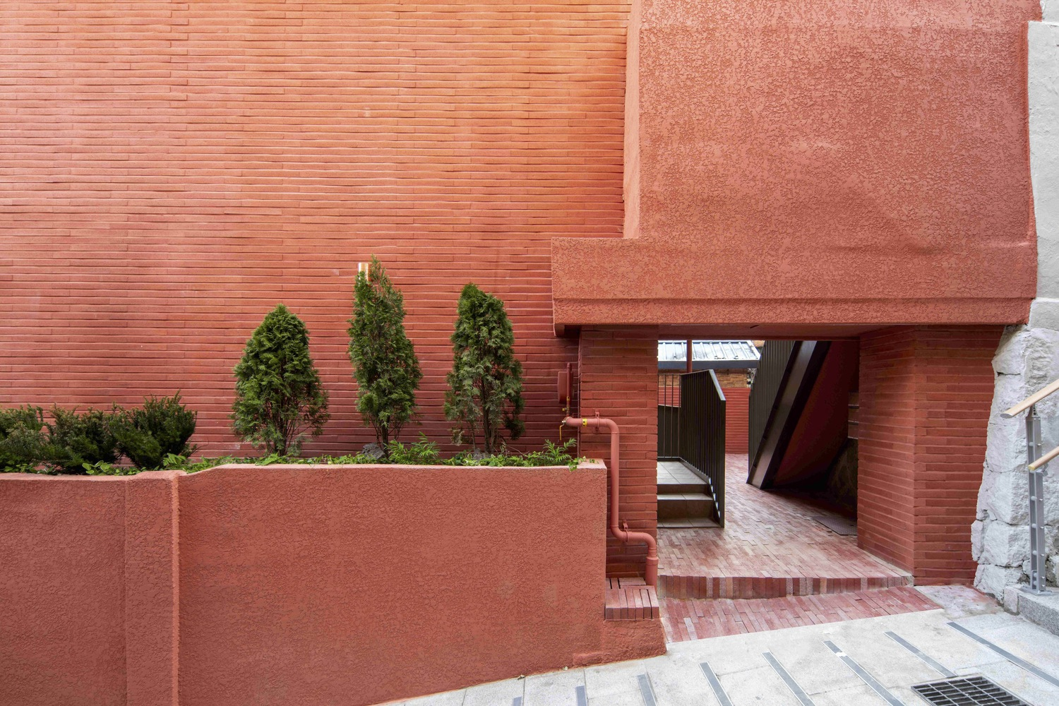 Red brick entry passage with planted bed of evergreen shrubs beside a low retaining wall