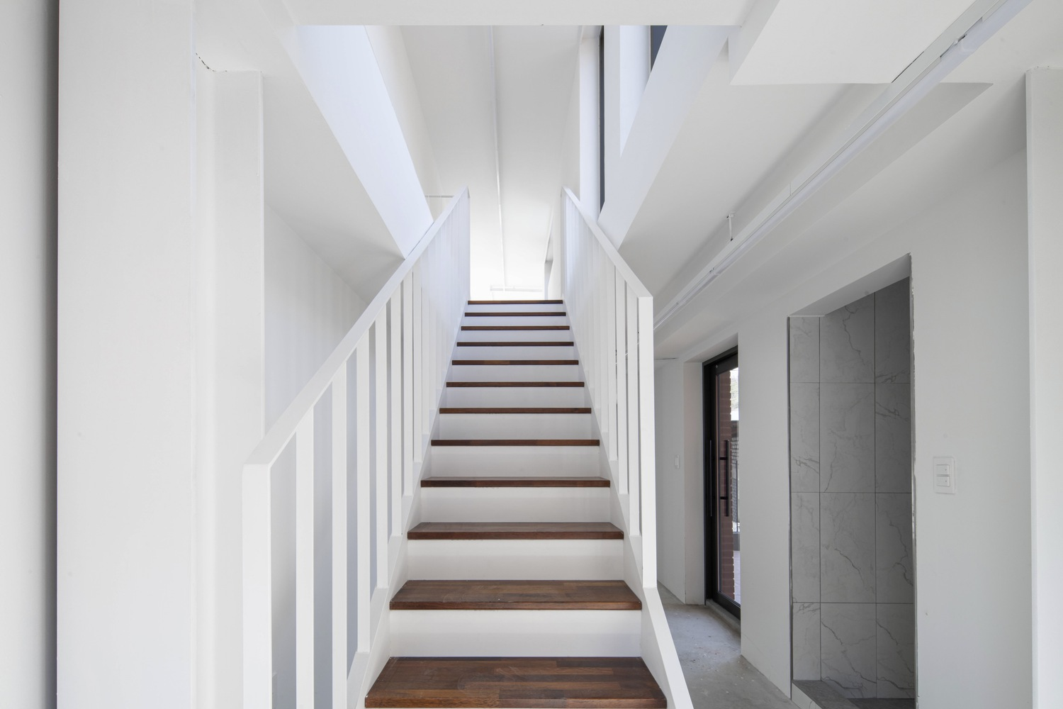 Interior staircase with white vertical railings and dark timber treads beneath angular skylight