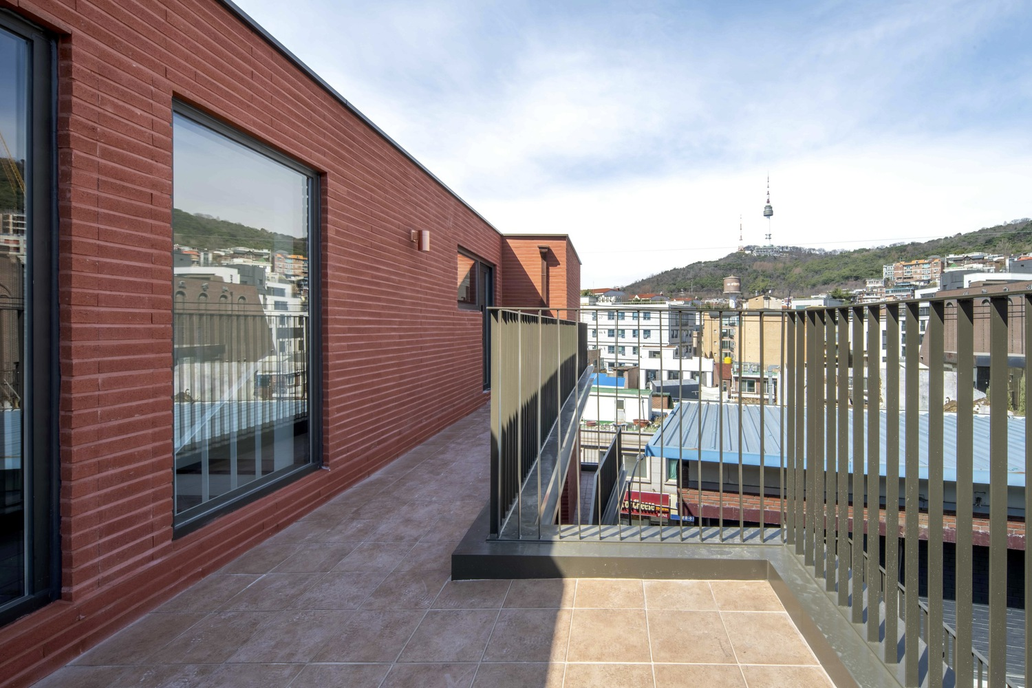 Rooftop terrace with red brick cladding and vertical wood slat railing overlooking hillside neighborhood