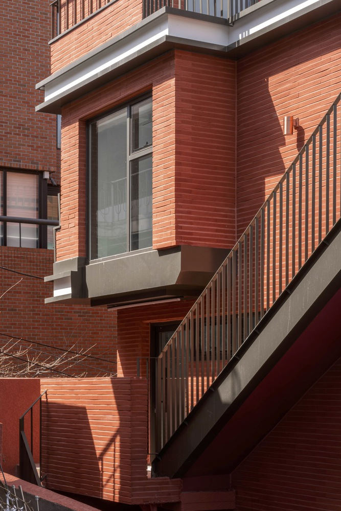 Corner detail of projecting window bay with horizontal brick panels and metal stair railing in bright light