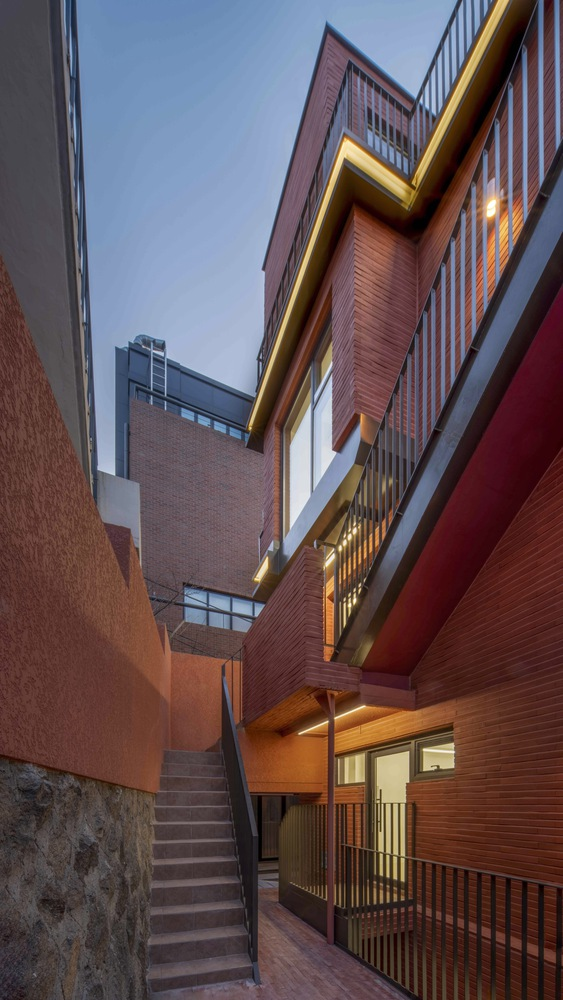 Narrow exterior stairway between red brick walls illuminated by uplighting at dusk