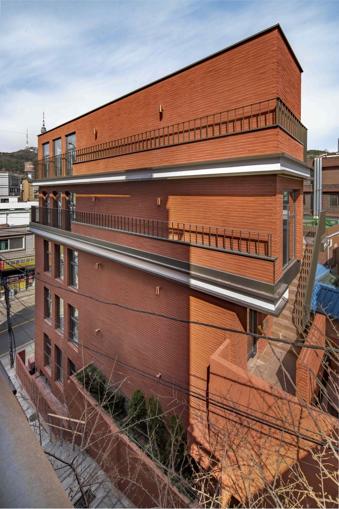 Street view of the stacked horizontal brick facade with recessed balconies and vertical wood screening