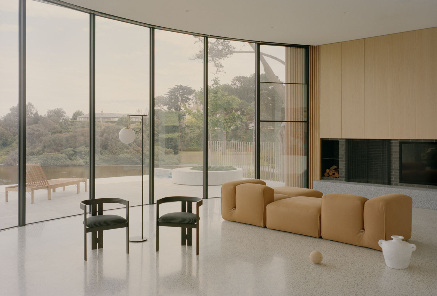 Living room with terrazzo flooring and full-height glazing opening to a terrace overlooking distant landscape in morning light