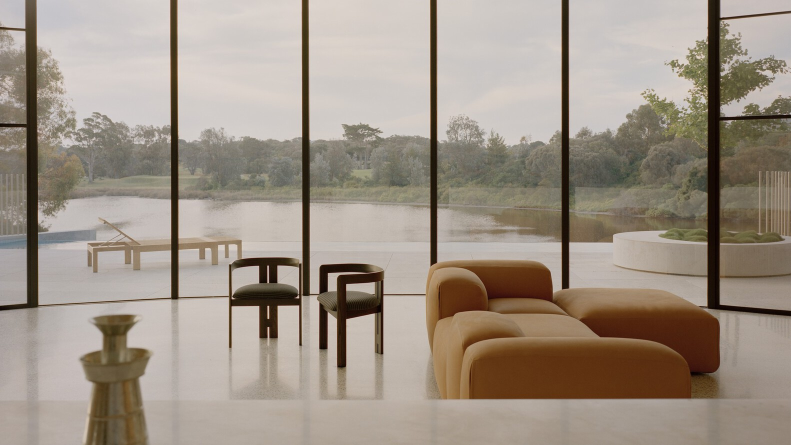 Glazed wall framing view of lake and wooded landscape with seating in foreground