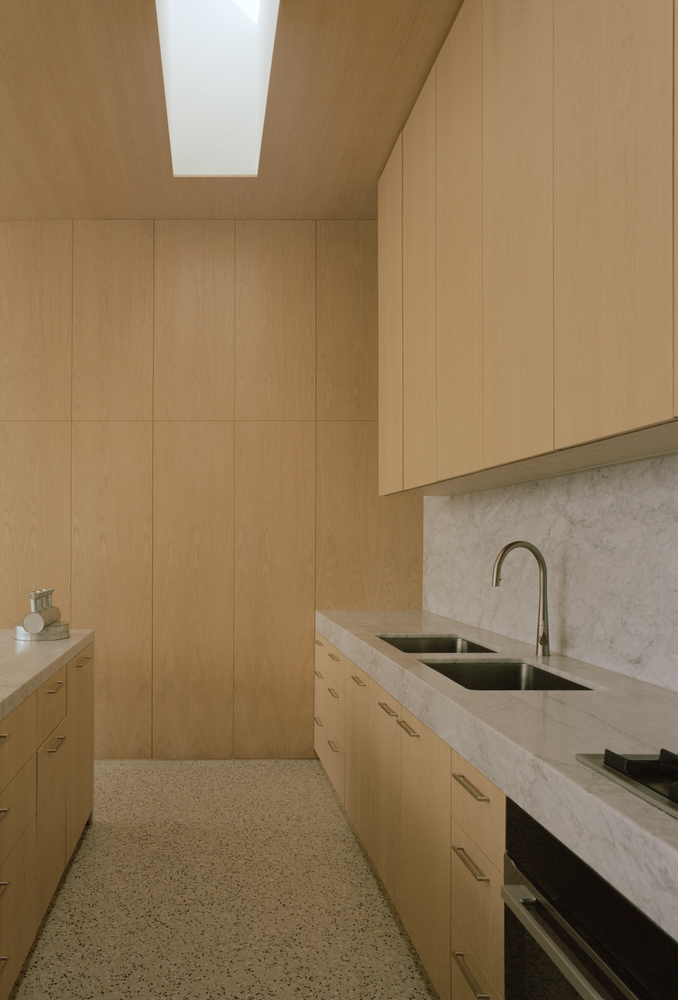 Galley kitchen with timber paneling and marble countertops illuminated by linear skylight