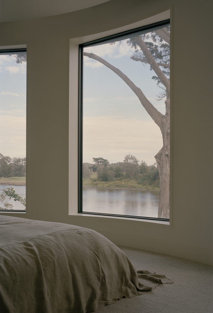 Bedroom window framing a leaning tree and distant river under an overcast sky